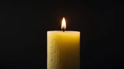 Eine brennende gelbe Kerze mit heller Flamme auf schwarzem Hintergrund als Symbol für Tod und Trauer.