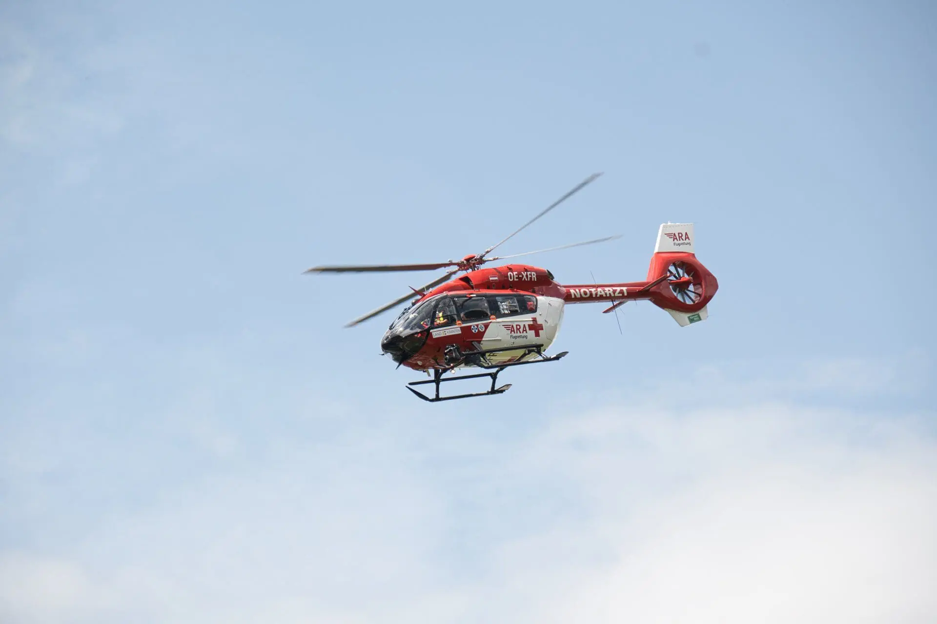 Roter und weißer Rettungshubschrauber der ARA Flugrettung im Flug vor blauem Himmel
