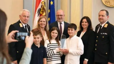 Kinder und Erwachsene posieren mit Glasaward im Landtagssaal vor Fahnen