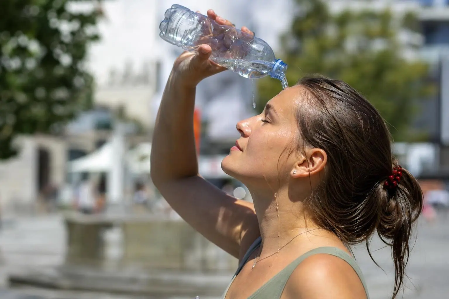 Eine Frau gießt Wasser aus einer Flasche über ihren Kopf zur Abkühlung