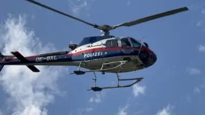 Polizeihubschrauber mit den Aufschriften POLIZEI und OE-BXL fliegt vor einem blauen Himmel mit Wolken.