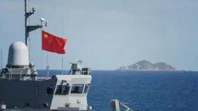 Chinesisches Kriegsschiff mit wehender Nationalflagge auf dem Meer vor einer Insel
