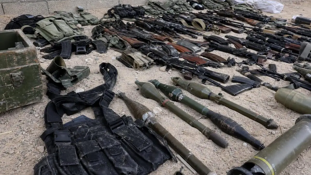 Zahlreiche Gewehre, Raketenwerfer und Munition liegen auf sandigem Boden ausgebreitet.