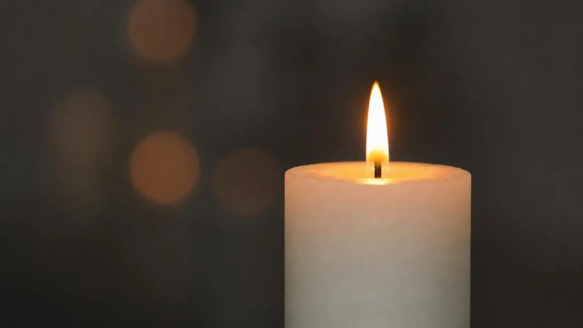 Brennende weiße Kerze mit warmer Flamme vor unscharfem dunklem Hintergrund