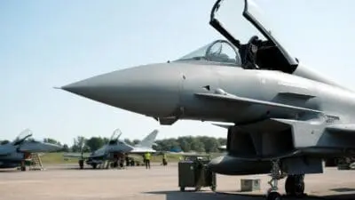 Grauer Eurofighter mit geöffneter Cockpit-Haube im Vordergrund, weitere Jets und Personal auf dem Rollfeld