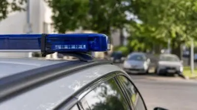 Blaues Blaulicht leuchtet auf dem Dach eines silbernen Polizeifahrzeugs auf einer Straße.