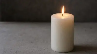Brennende weiße Stumpenkerze steht auf einer grauen Oberfläche vor dunklem Hintergrund