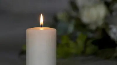 Brennende weiße Kerze im Vordergrund, unscharfe Blumen im Hintergrund