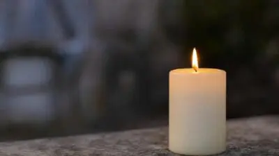 Weiße brennende Stumpenkerze mit gelber Flamme auf steinerner Fläche