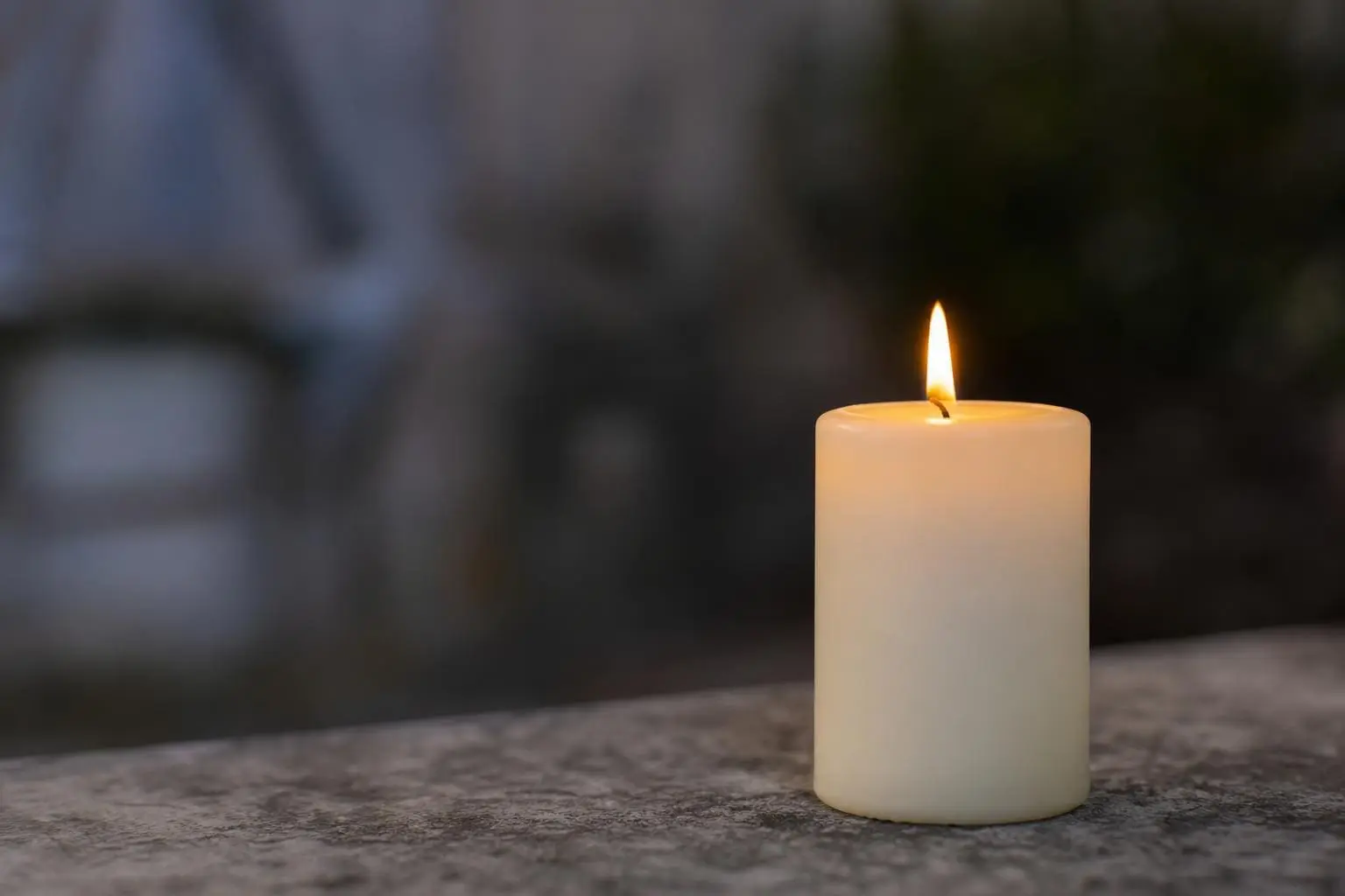 Weiße brennende Stumpenkerze mit gelber Flamme auf steinerner Fläche