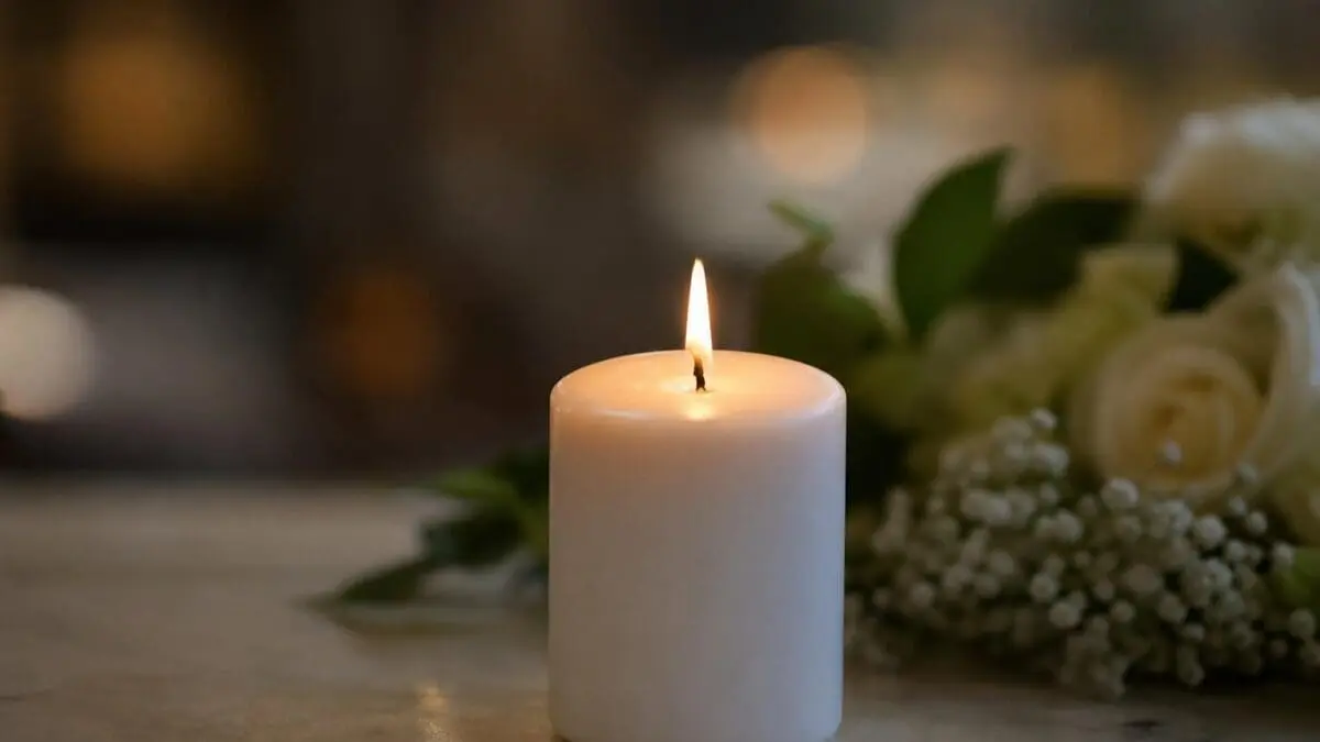 Eine brennende weiße Kerze auf einer Marmorplatte neben weißen Rosen und Schleierkraut