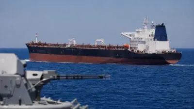 Großer Öltanker fährt auf blauem Meer, im Vordergrund unscharf ein Schiffsgeschütz