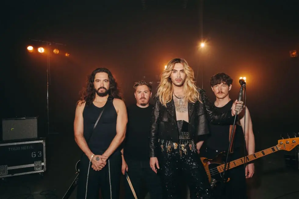 Vier Mitglieder der Band Tokio Hotel stehen auf einer dunklen Bühne mit Scheinwerfern.