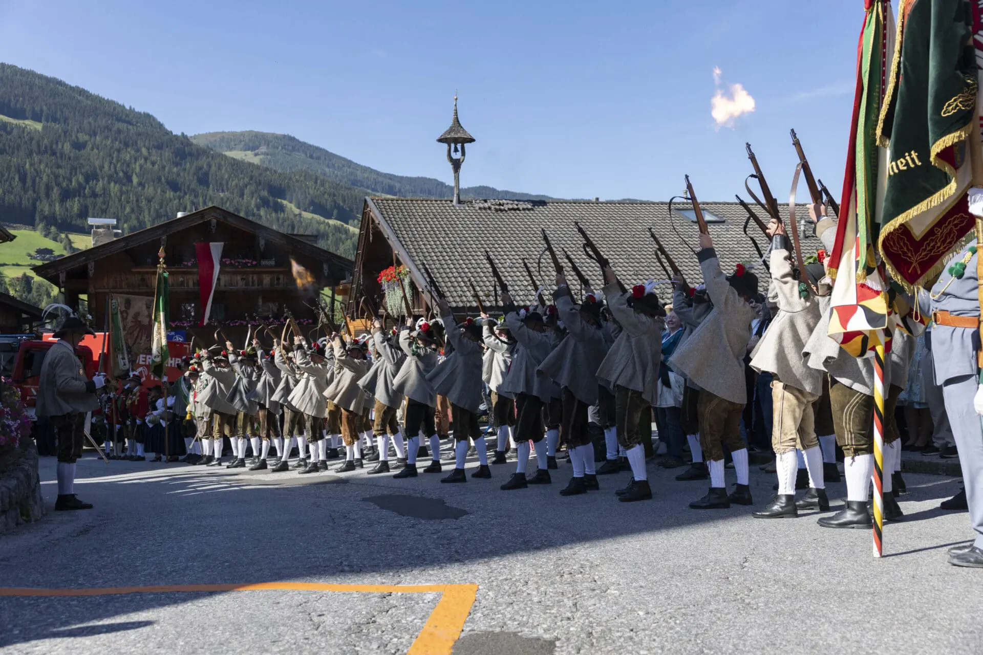 Schützen in Tracht schießen mit erhobenen Gewehren bei einer Veranstaltung in Alpbach.