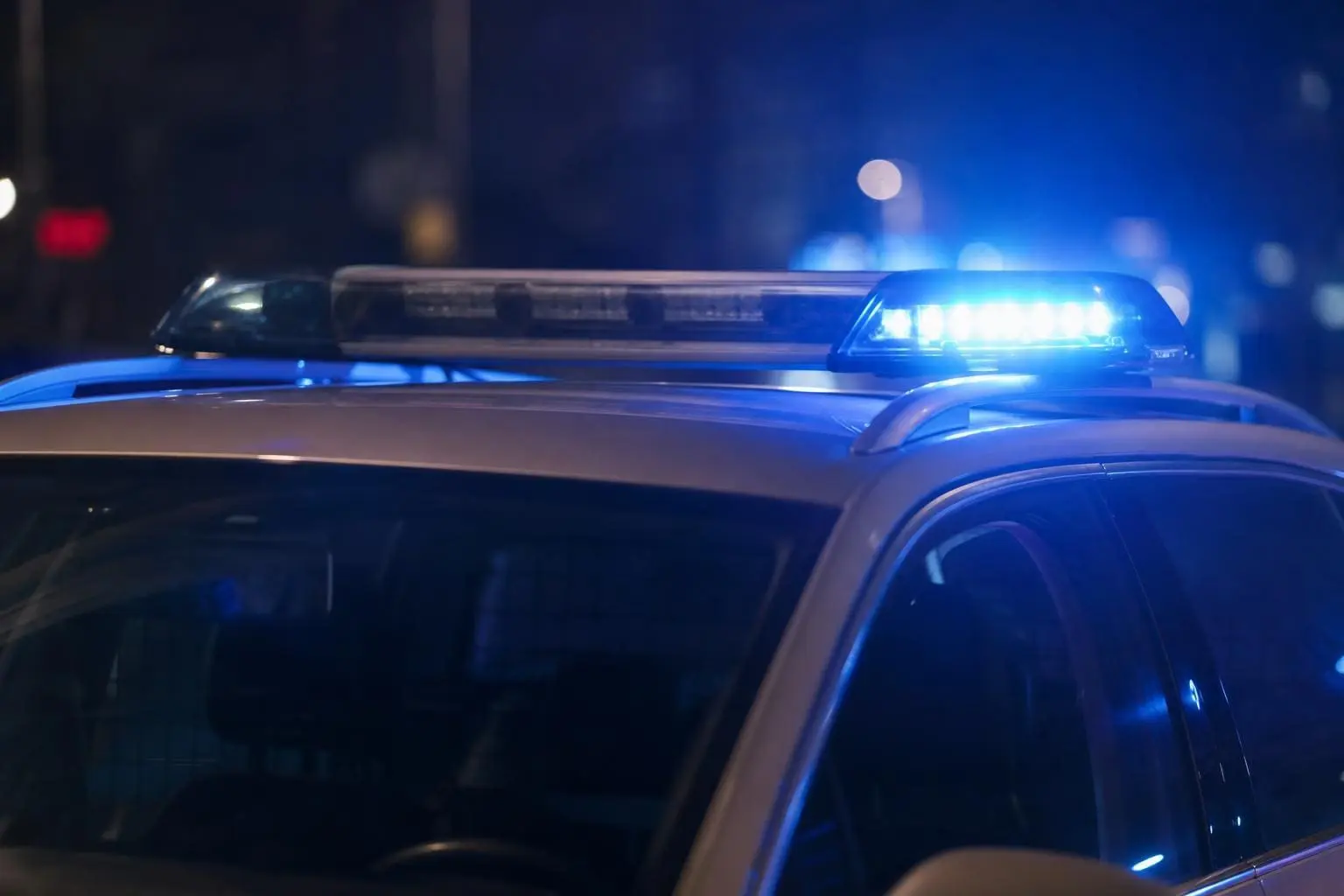 Nahaufnahme eines Polizeifahrzeugs mit blauem Blaulichtbalken auf dem Dach bei Nacht