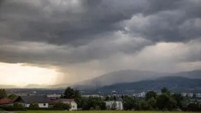 Dunkle Gewitterwolken über einer Stadt mit umliegenden Bergen und Häusern im Vordergrund