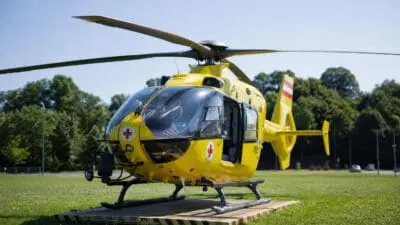Gelber Rettungshubschrauber mit roten Kreuzen und geöffneter Tür auf einer Wiese