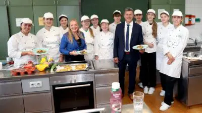 Landeshauptmann Daniel Fellner und Schülerinnen und Schüler präsentieren Speisen in einer Lehrküche.