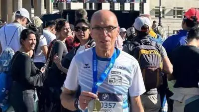Angelo Quaglia mit Medaille und Startnummer beim Berlin-Marathon, umgeben von Läuferinnen und Läufern.