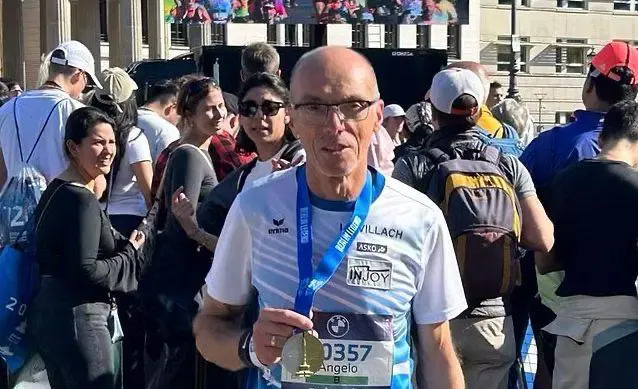 Angelo Quaglia mit Medaille und Startnummer beim Berlin-Marathon, umgeben von Läuferinnen und Läufern.