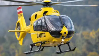 Gelber ÖAMTC-Hubschrauber fliegt vor einer bewaldeten Landschaft.