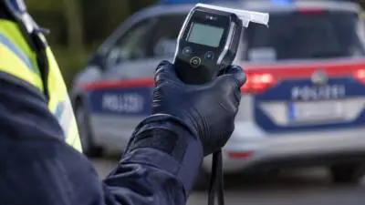 Polizeibediensteter hält ein Messgerät vor einem Streifenwagen.