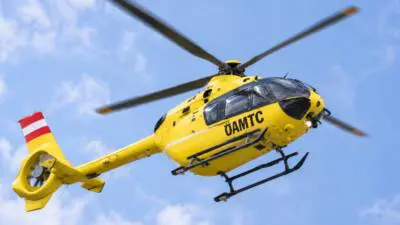 Gelber ÖAMTC-Hubschrauber mit Rotoren vor blauem Himmel mit Wolken
