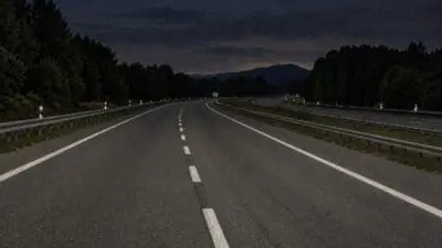 Leere Autobahn bei Nacht mit weißen Markierungen und Leitplanken zwischen bewaldeten Hängen.