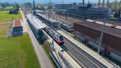 Luftaufnahme des modernisierten Bahnhofs Wolfurt mit Bahnsteigen, Gleisen und einem Zug
