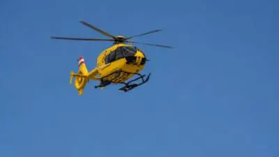 Gelber Rettungshubschrauber fliegt vor blauem Himmel als Symbolbild zum Verkehrsunfall.