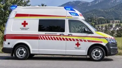 Weißer Rettungswagen des Österreichischen Roten Kreuzes mit Blaulicht und roten Warnstreifen vor Berglandschaft