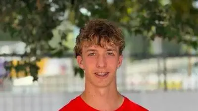 Junger Mann mit braunem Haar in rotem T-Shirt lächelt mit Zahnspange in die Kamera