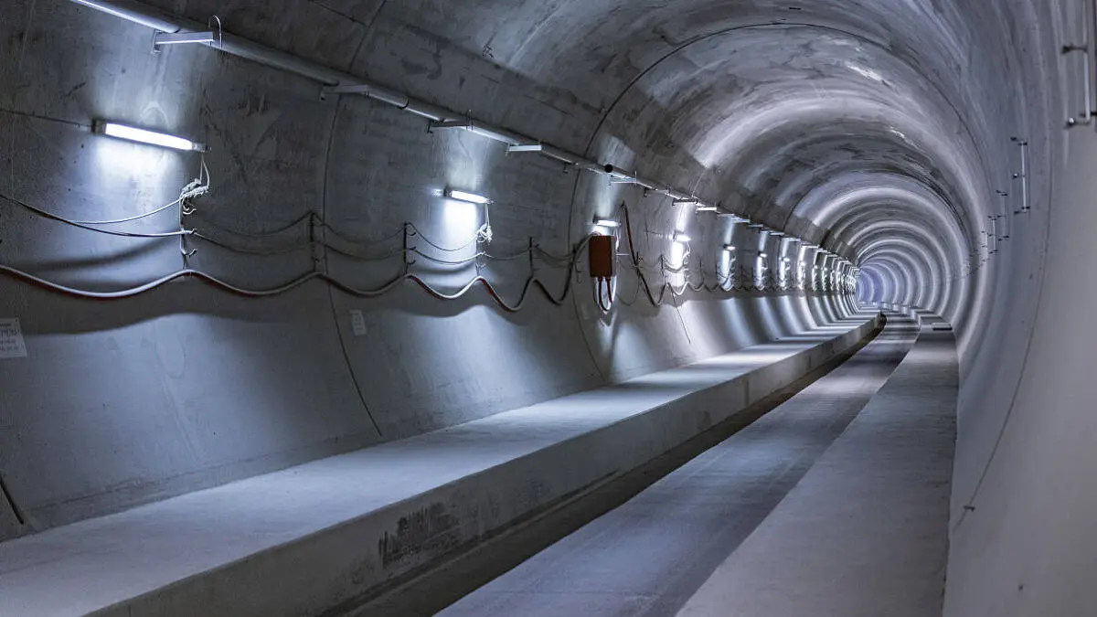 Beleuchteter Betonbahntunnel mit Kabeln und seitlichen Wartungswegen