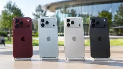 Rückansicht von vier iPhone-Modellen in Rot, Hellgrau, Silber und Schwarz auf einer Holzfläche.