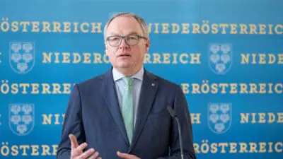 Ein Mann mit Brille in einem dunklen Anzug und grüner Krawatte gestikuliert an einem Rednerpult.