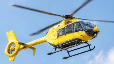 Ein gelber Hubschrauber fliegt vor blauem Himmel.