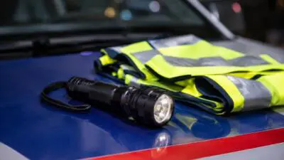 KI-generiertes Bild: Eine schwarze Taschenlampe und eine gelbe Warnweste liegen auf einer blau-roten Fahrzeugoberfläche.