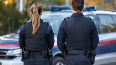 KI-Symbolbild: Uniformierte Personen stehen vor einem blau-weißen Fahrzeug mit Blaulicht.