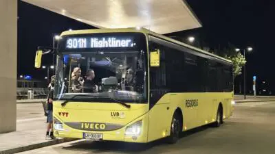 Gelber Nightliner-Bus der Linie 900N mit Fahrgästen im Innenraum steht nachts unter einem beleuchteten Dach.