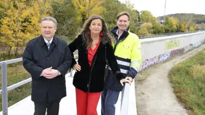 Personen stehen auf einem Steg neben einer Betonwand und einem Geländer.
