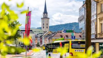 Gelber Villacher Stadtbus fährt an Häusern und einem Kirchturm vorbei