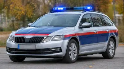 KI-Symbolbild: Ein silberner Kombi mit blauem Blaulicht und rot-blauen Streifen auf einer Straße.