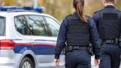 KI-generiertes Bild: Uniformierte Personen stehen neben einem weiß-blauen Wagen mit Blaulicht.