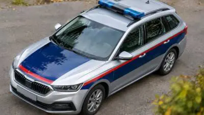 KI-Symbolbild: Ein silberner Kombi mit blau-roten Streifen und Blaulicht steht auf einem Weg.
