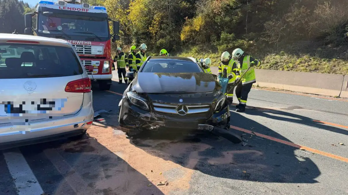 Feuerwehrleute stehen neben einem beschädigten Pkw und einem Feuerwehrfahrzeug auf der Straße.