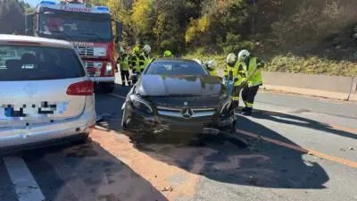 Feuerwehrleute stehen neben einem beschädigten Pkw und einem Feuerwehrfahrzeug auf der Straße.