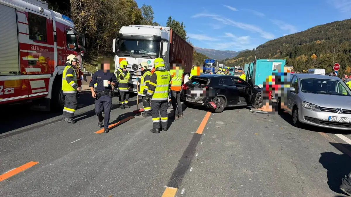Feuerwehrleute und Einsatzkräfte stehen neben Lastwagen und beschädigten Autos auf einer Straße.
