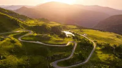 Eine kurvenreiche Bergstraße windet sich durch grüne Nockberge im Abendlicht.