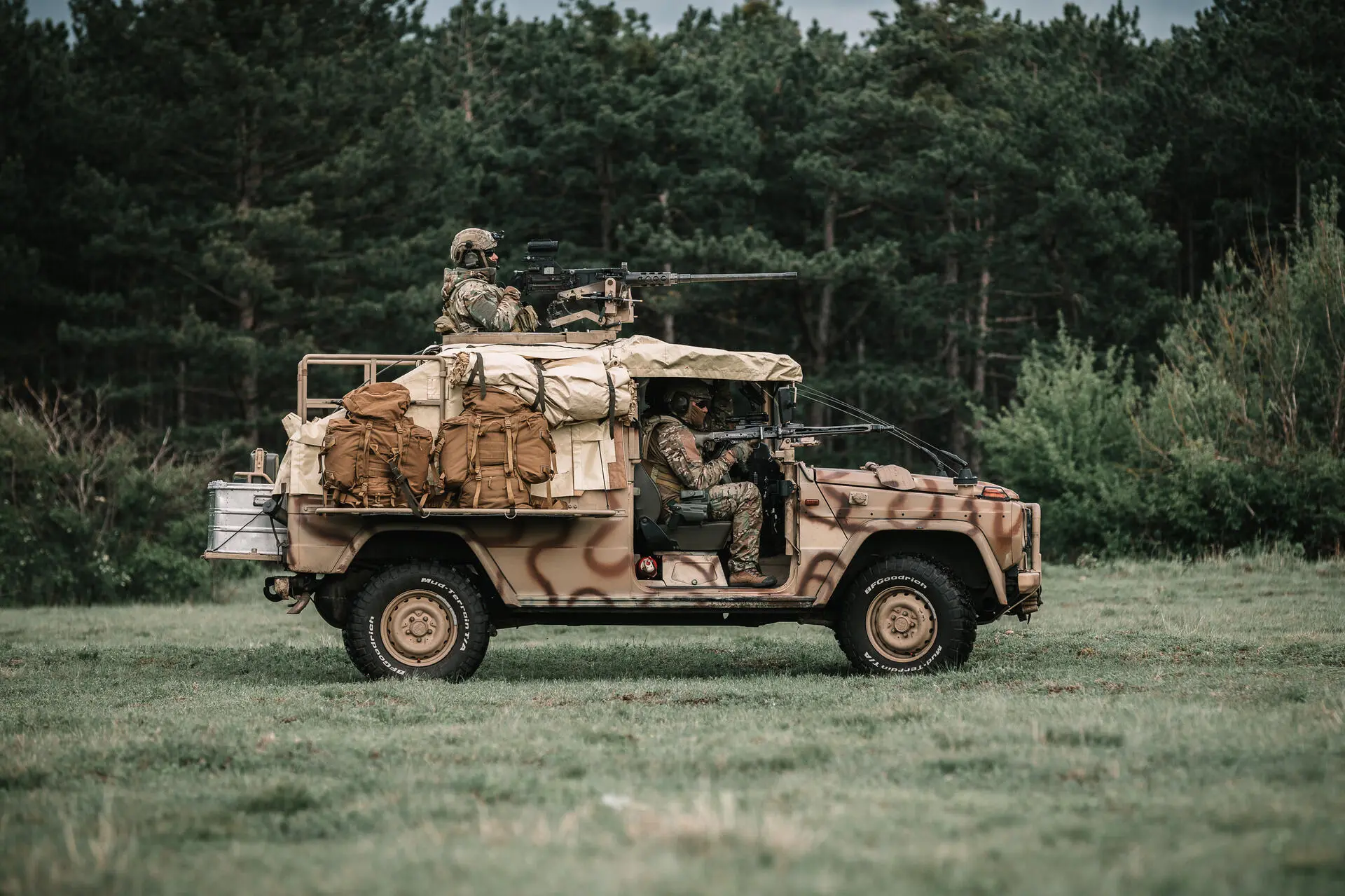 Soldaten sitzen auf einem getarnten Geländewagen mit aufmontierten Waffen vor einem Wald.