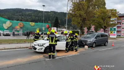 Feuerwehrleute arbeiten neben einem weißen Auto und einem grauen Van auf der Straße.